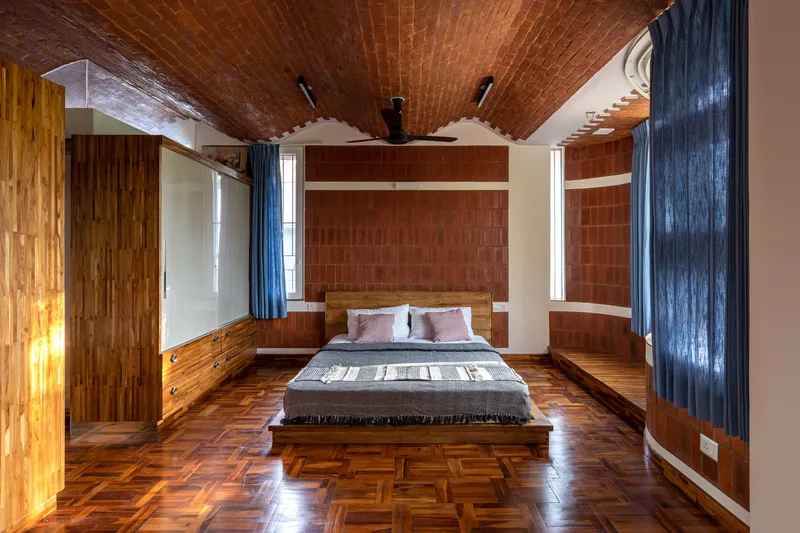 Bedroom with herringbone wood floor, red clay tile walls, and vaulted brick ceiling with exposed rafters