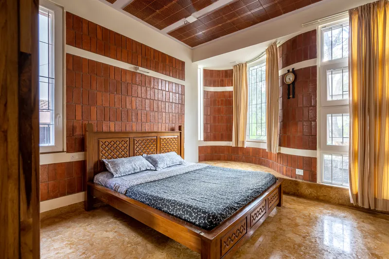 Bedroom with curved bay window, red tile walls, and timber plank ceiling in daylight
