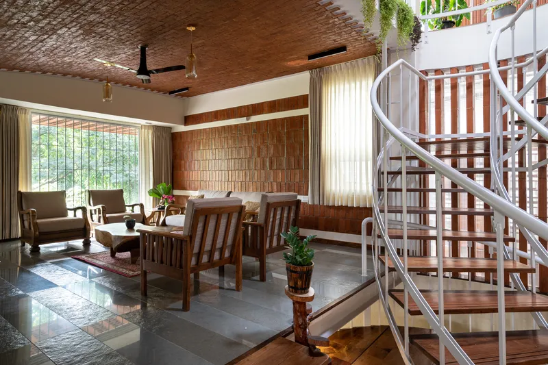 Living area with spiral metal staircase, brick ceiling, and upholstered chairs near a garden window