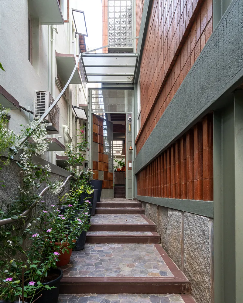 Narrow entrance passage with timber-framed steps, terracotta pavers and potted plants under a glass canopy