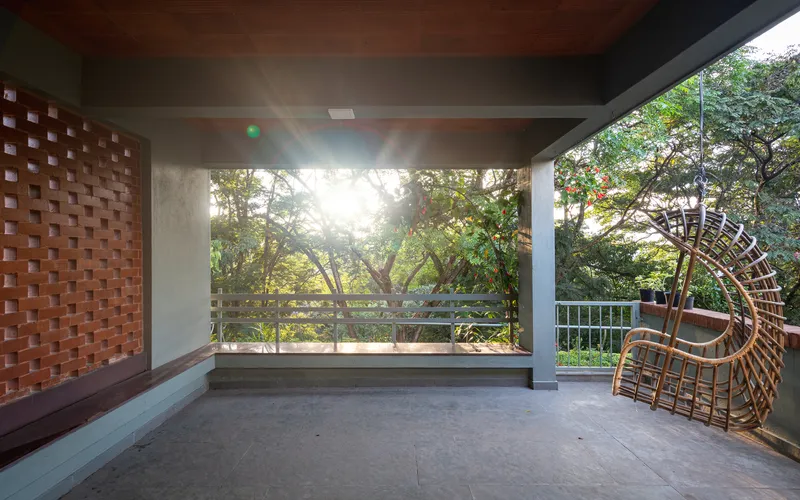 Open terrace with chequered brick screen wall, concrete soffit and wicker chair facing treetops
