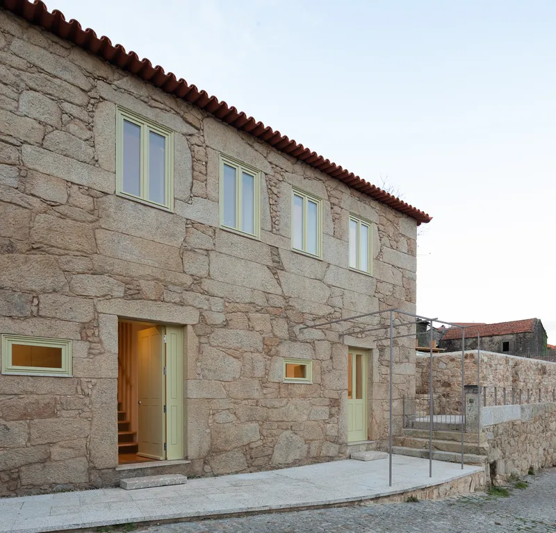 Street facade of granite stone walls with red clay tile roof and pale green windows at dusk