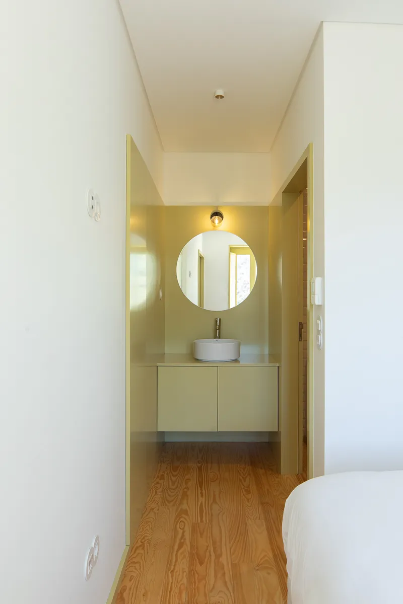 Narrow bathroom entry with round mirror above vessel sink and pale green walls