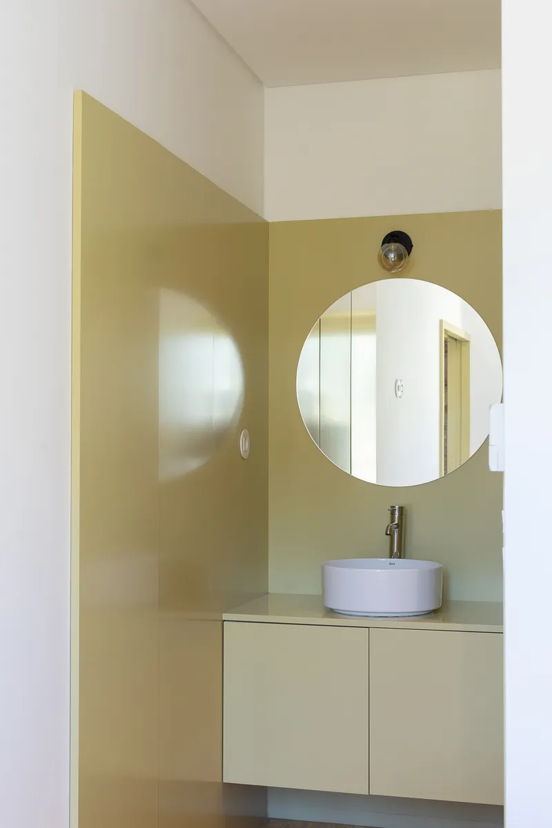 Bathroom vanity with circular mirror and vessel sink set against pale green tile