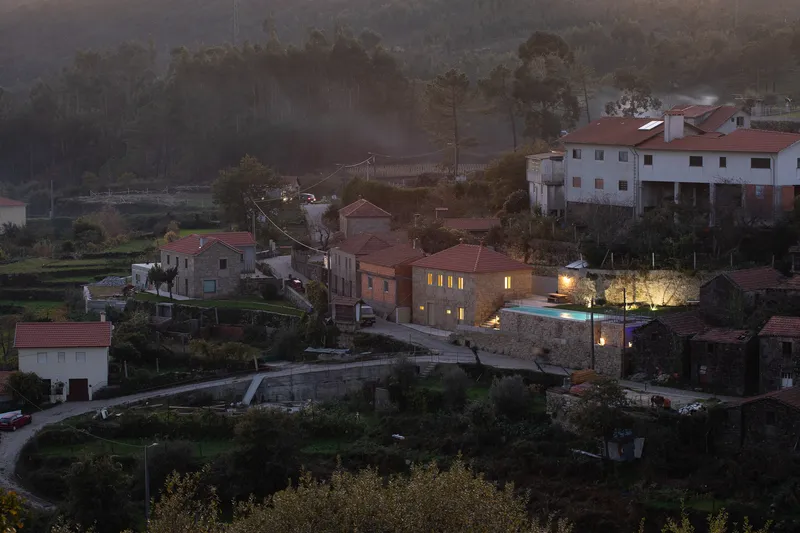 Stone house illuminated among clustered village buildings on a hillside at dusk with mist