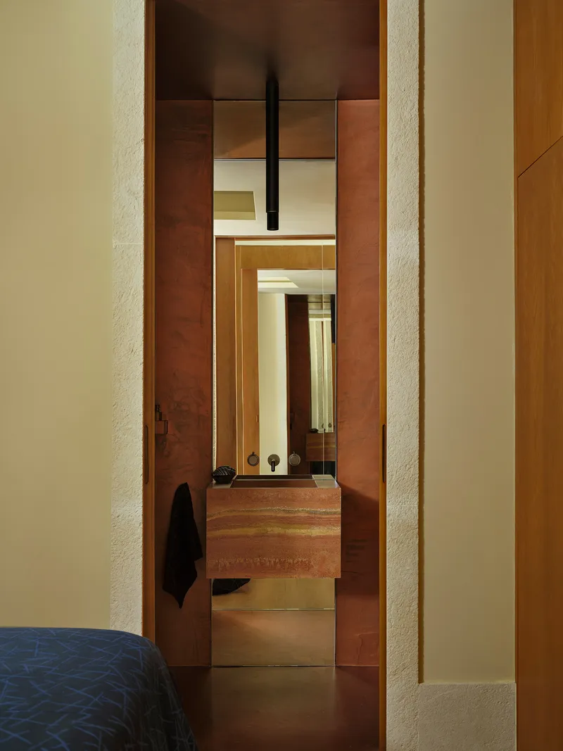 View through layered doorways framed in timber and red stone into an ensuite bathroom