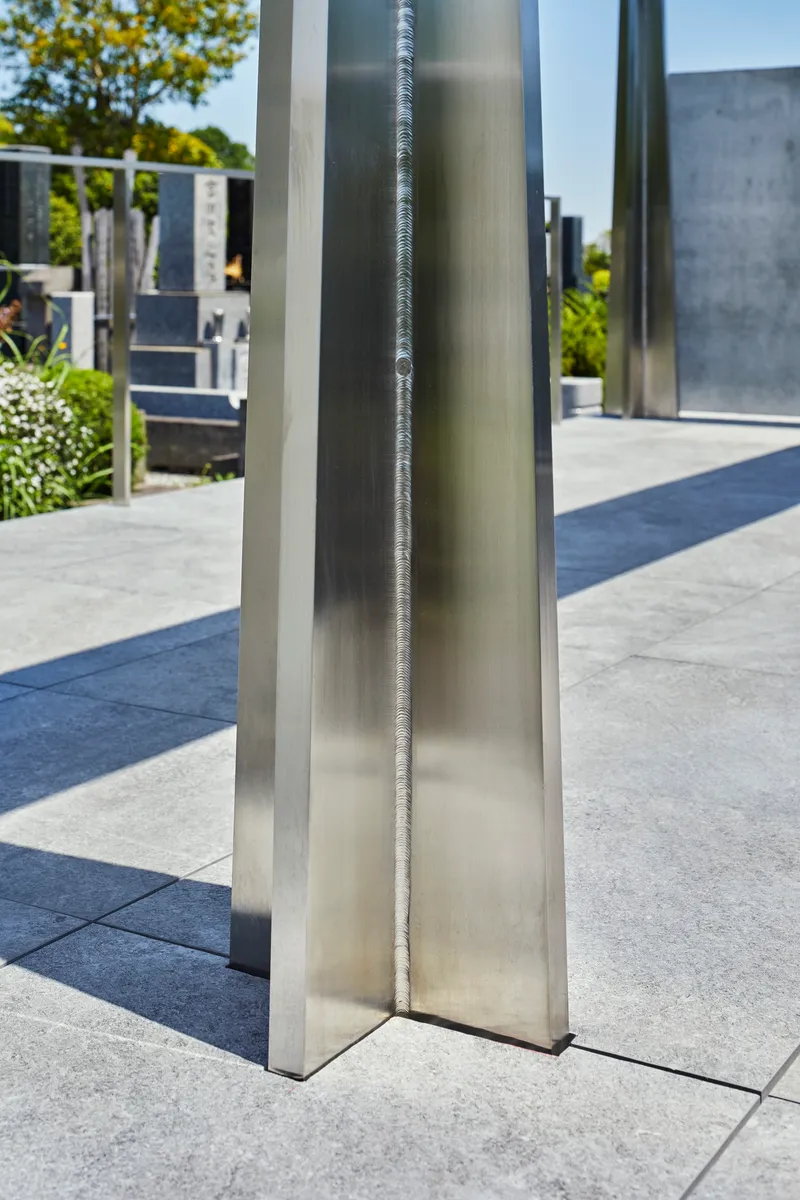 Close-up of a polished stainless steel column with exposed welded seam in bright daylight