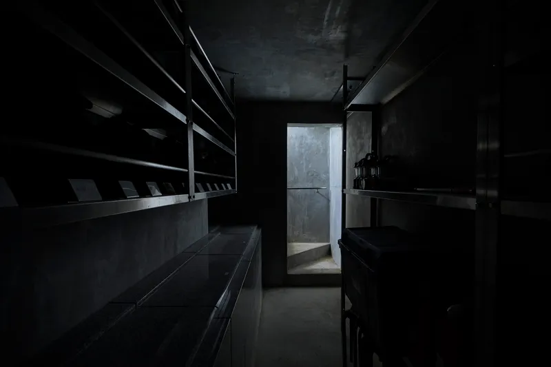 Dark interior corridor with steel shelving along walls and doorway backlit by diffused light