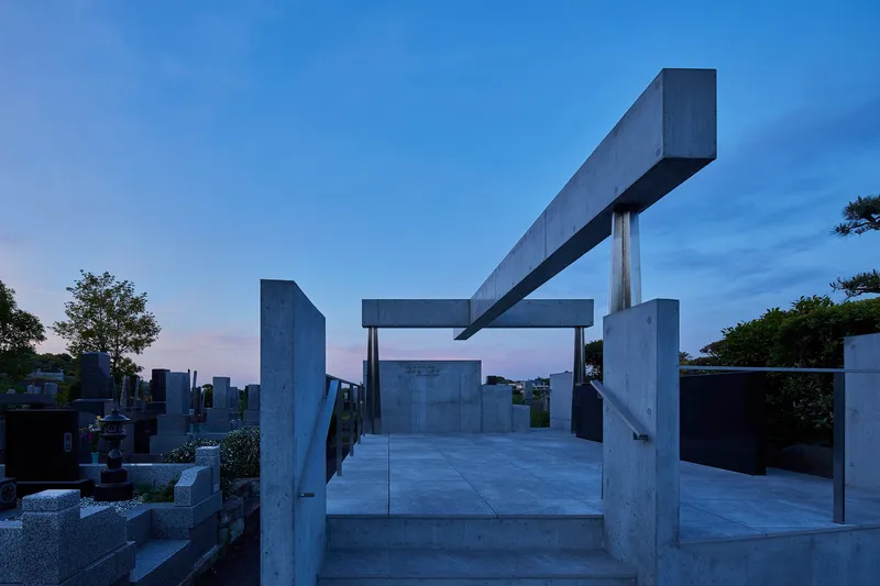 Concrete pavilion with overhead beam structure photographed at dusk with pink sky behind