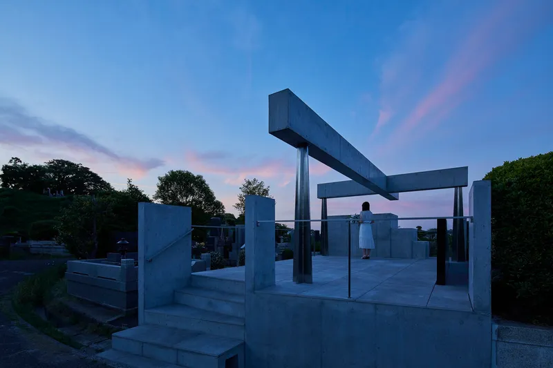 Open concrete platform with columns and beams as a figure stands beneath at twilight