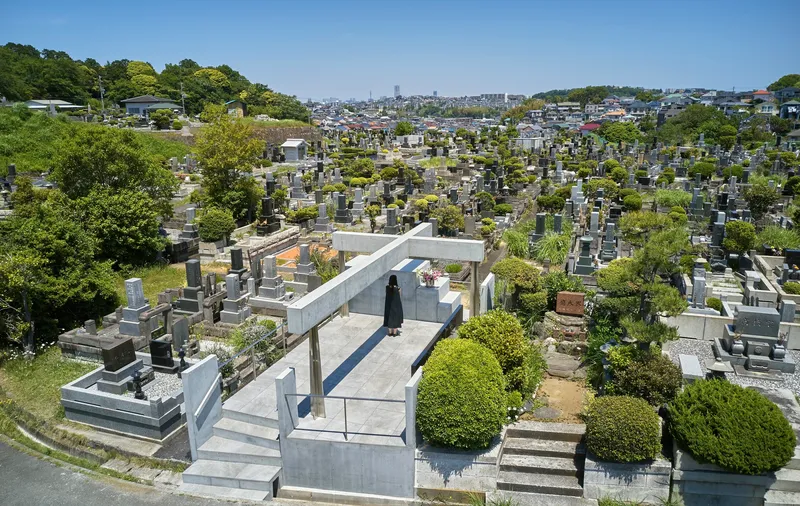 Elevated view of the concrete memorial structure surrounded by traditional gravestones and mature trees in a hillside cemetery