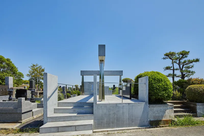 Concrete memorial platform with vertical columns supporting horizontal beams framing a glass monument under clear blue sky