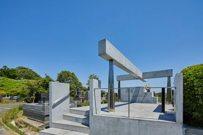 Corner perspective of the stepped concrete base and cantilevered beam structure with glass enclosure among cemetery plots