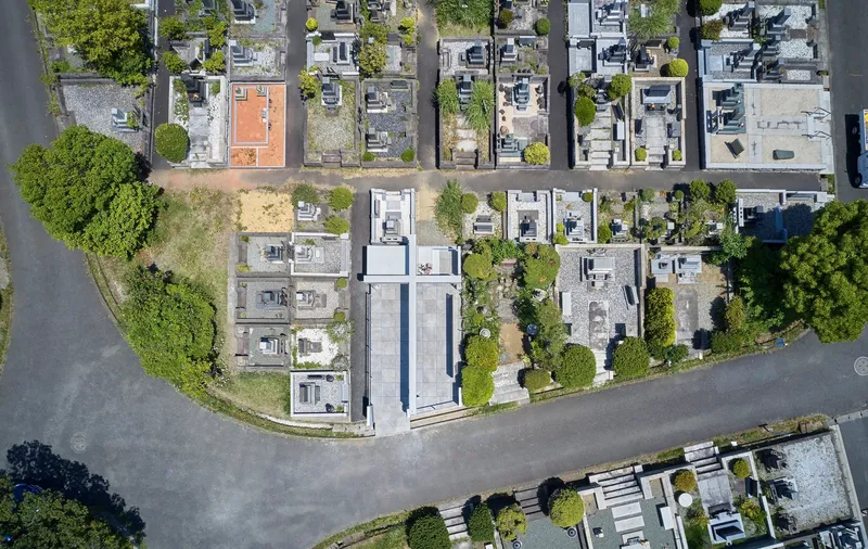 Aerial view of the cruciform concrete memorial centered within its rectangular plot at a curved cemetery road junction