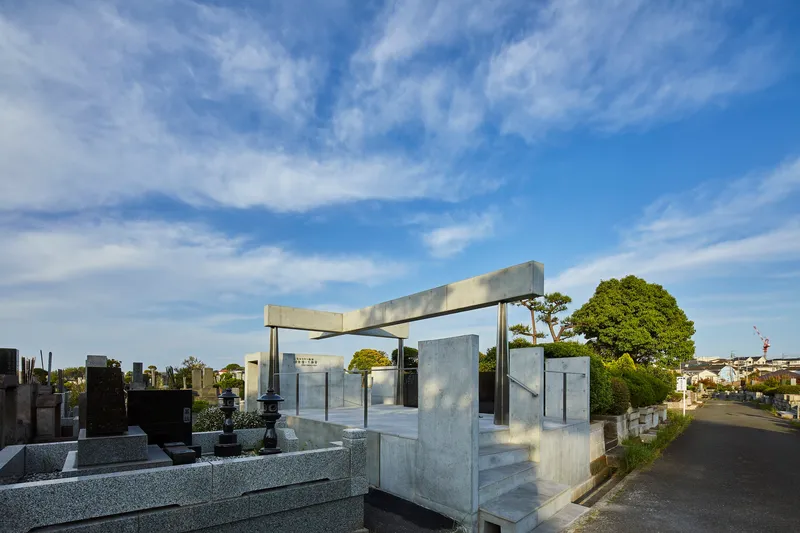 Concrete memorial structure with elevated beam and steel columns among cemetery plots under afternoon sky