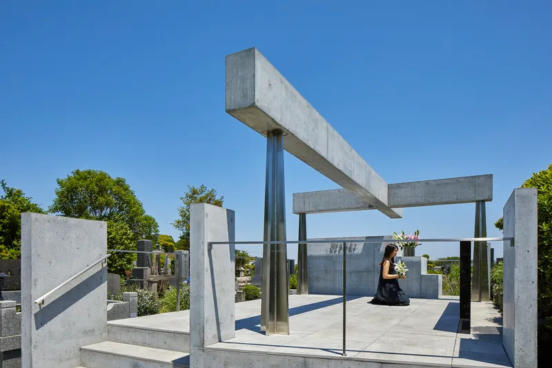 Person kneeling on concrete platform beneath intersecting beams and steel columns with glass balustrade