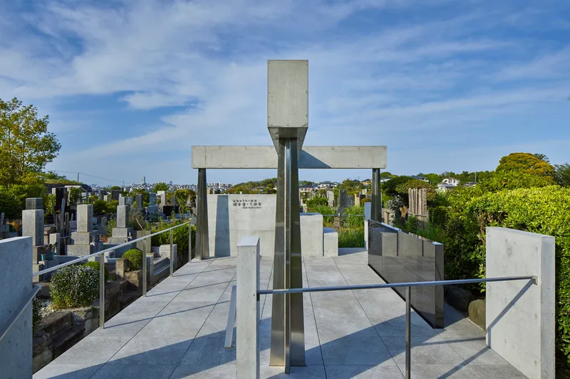 Concrete cross-shaped structure with steel columns and central monument stone overlooking cemetery landscape