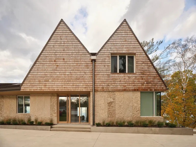 Entrance facade with twin gabled cedar shingle roofs above rammed earth walls and concrete terrace