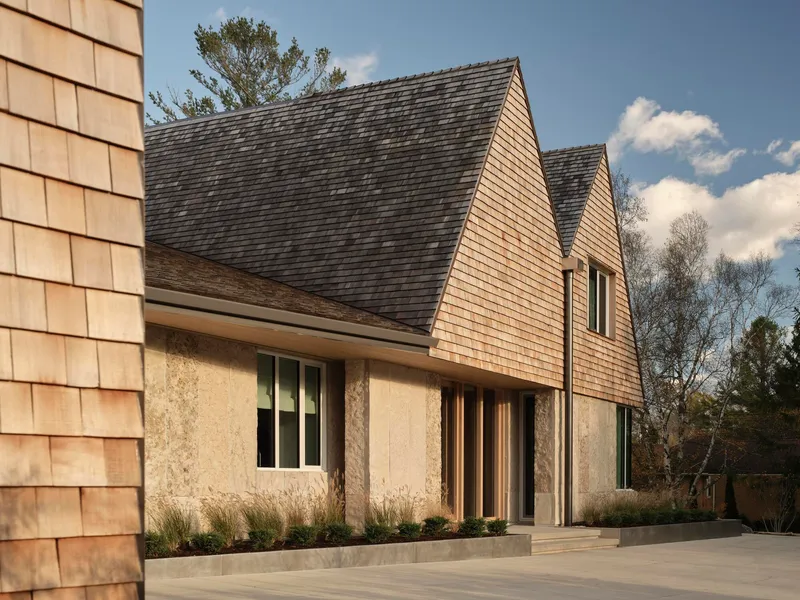 Side elevation showing the layered gable roofs with cedar shingles above textured rammed earth walls
