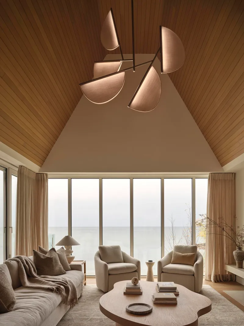 Living room with vaulted timber ceiling and glazed wall overlooking the water under overcast skies