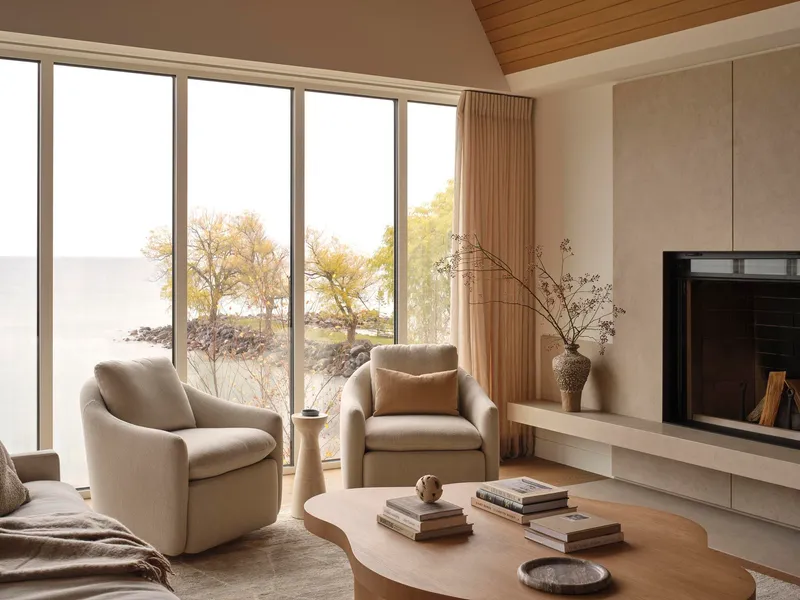 Seating area with fireplace hearth and floor-to-ceiling windows framing autumn trees along the shoreline