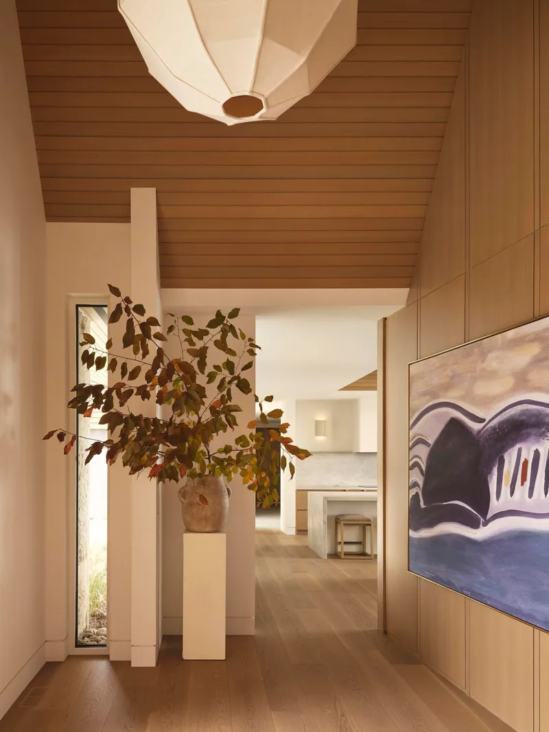 Hallway with horizontal wood ceiling and sculptural pendant light above a branching arrangement in terracotta vessel