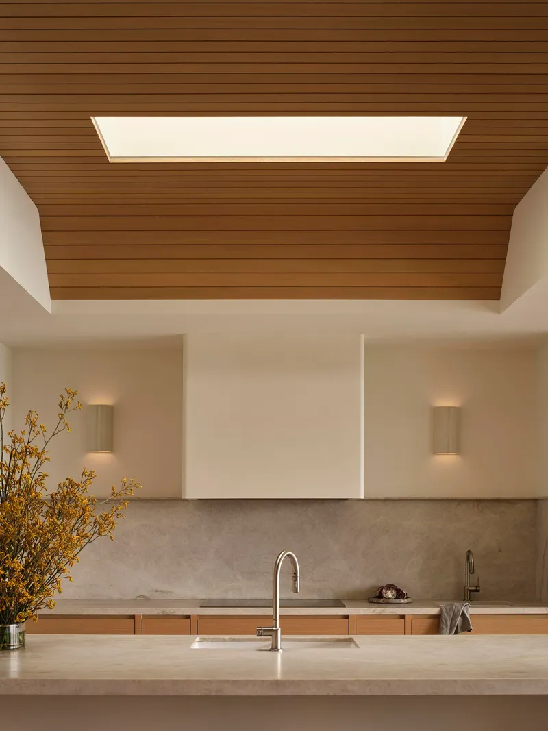 Kitchen island with stone countertop under a timber ceiling panel with integrated skylight