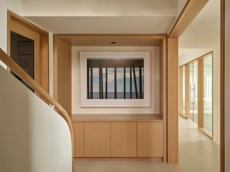 Light oak corridor with timber-framed window opening and built-in cabinets beneath a curved stairwell