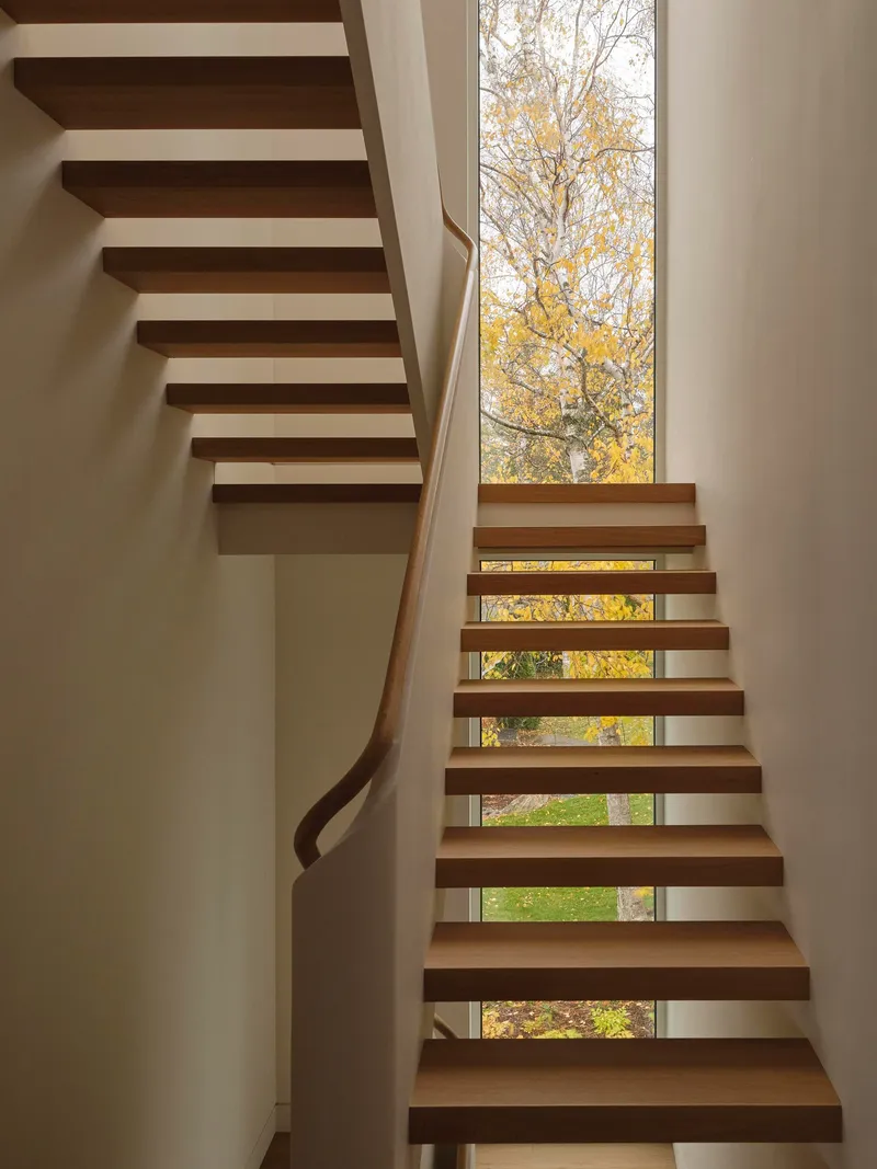 Open-riser timber staircase with horizontal window slots framing autumn trees outside