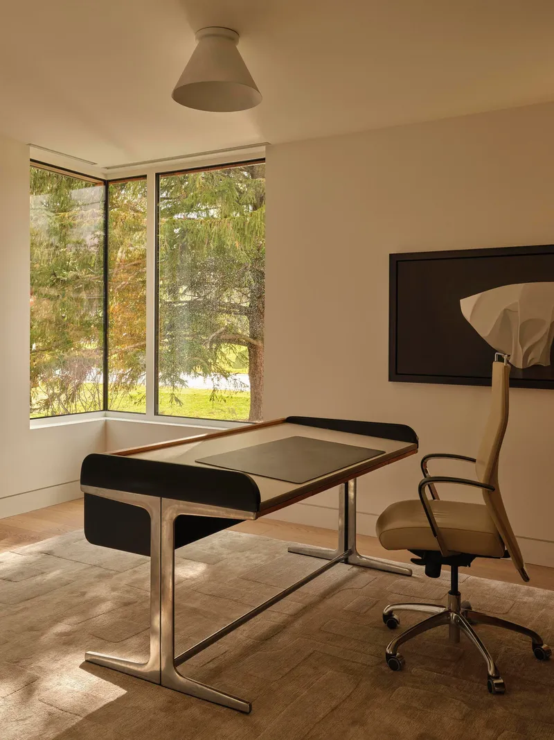 Corner study with black-framed desk and tall window overlooking trees in afternoon light