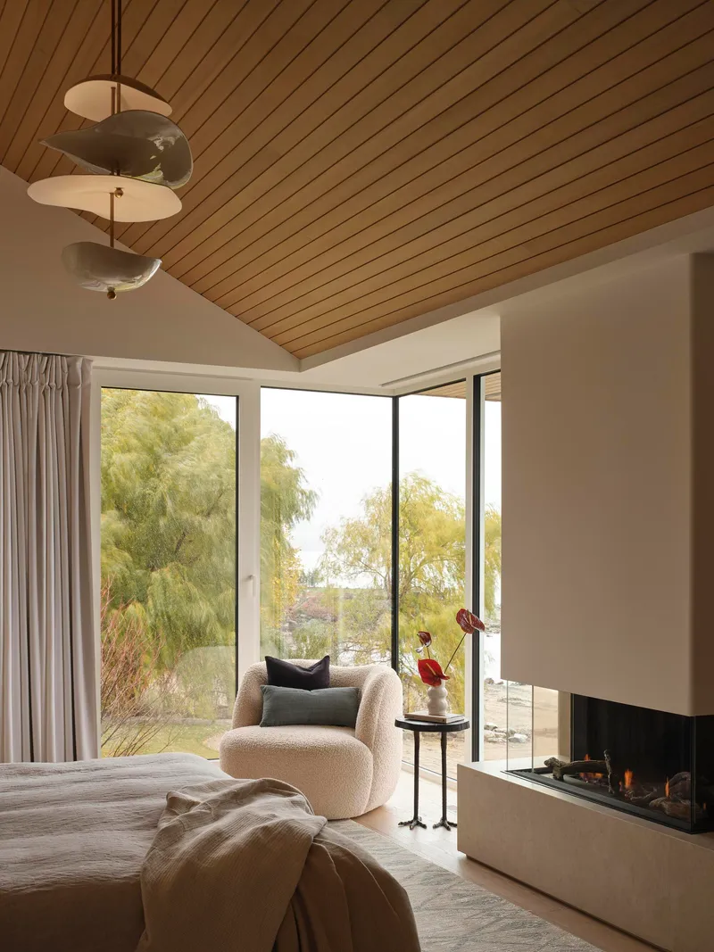 Bedroom with timber slat ceiling and corner glazing opening to garden foliage and fireplace