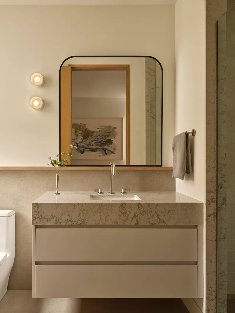 Floating vanity with thick stone countertop beneath a rounded-corner mirror and two circular wall sconces
