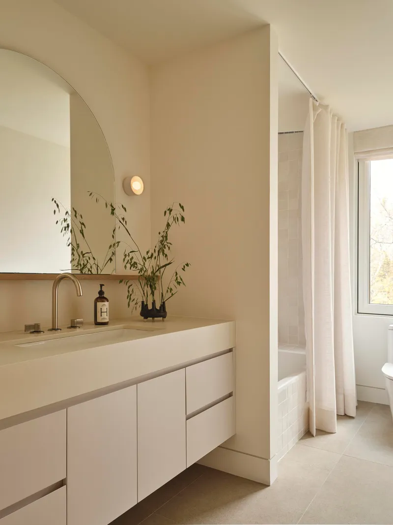 Bathroom vanity with arched mirror and dried grasses in a vase beside the window