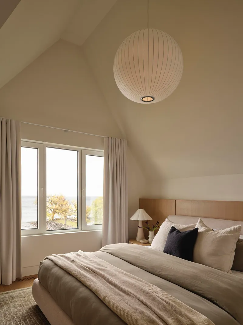 Bedroom with vaulted ceiling and spherical pendant light above a window overlooking the water