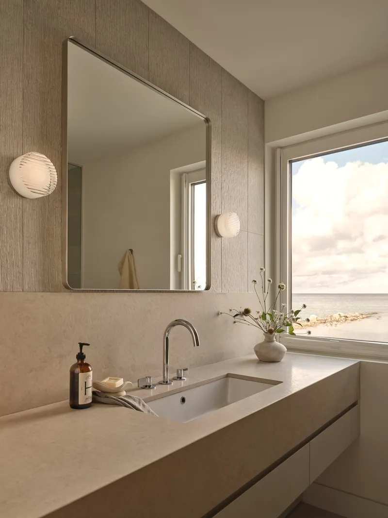 Vanity counter with textured wall panel and square mirror reflecting the ocean view window