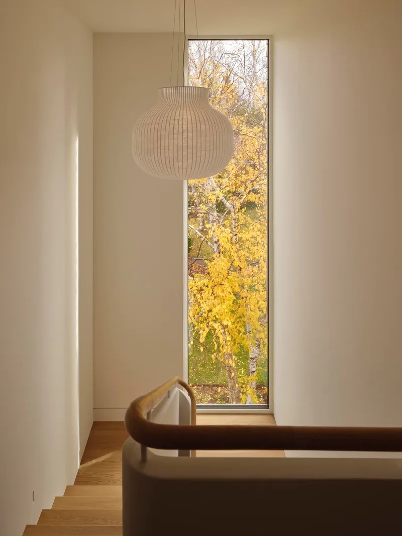 Tall window framing yellow autumn foliage with a ribbed pendant light and timber stair handrail
