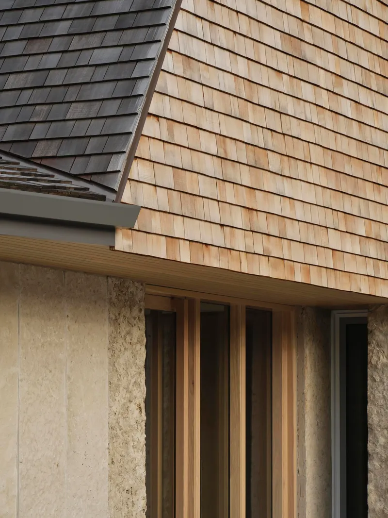 Detail of wood shingle cladding meeting a stone base below a timber-framed window