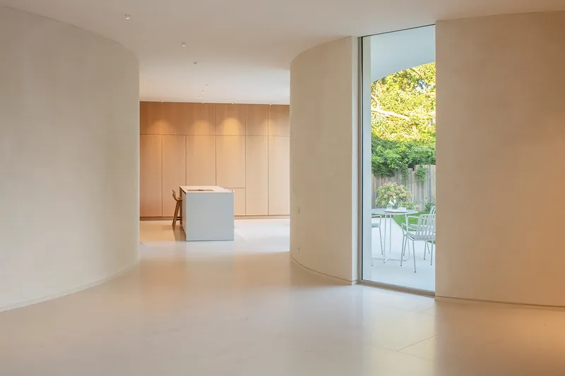 Interior view through curved archway to kitchen with timber cabinetry and garden beyond glass wall
