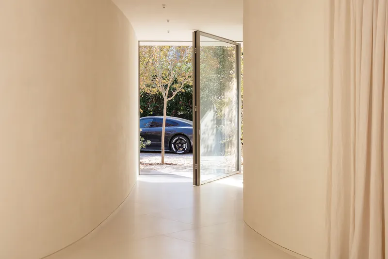 Curved hallway entrance with glass pivot door framing a blue car and tree outside