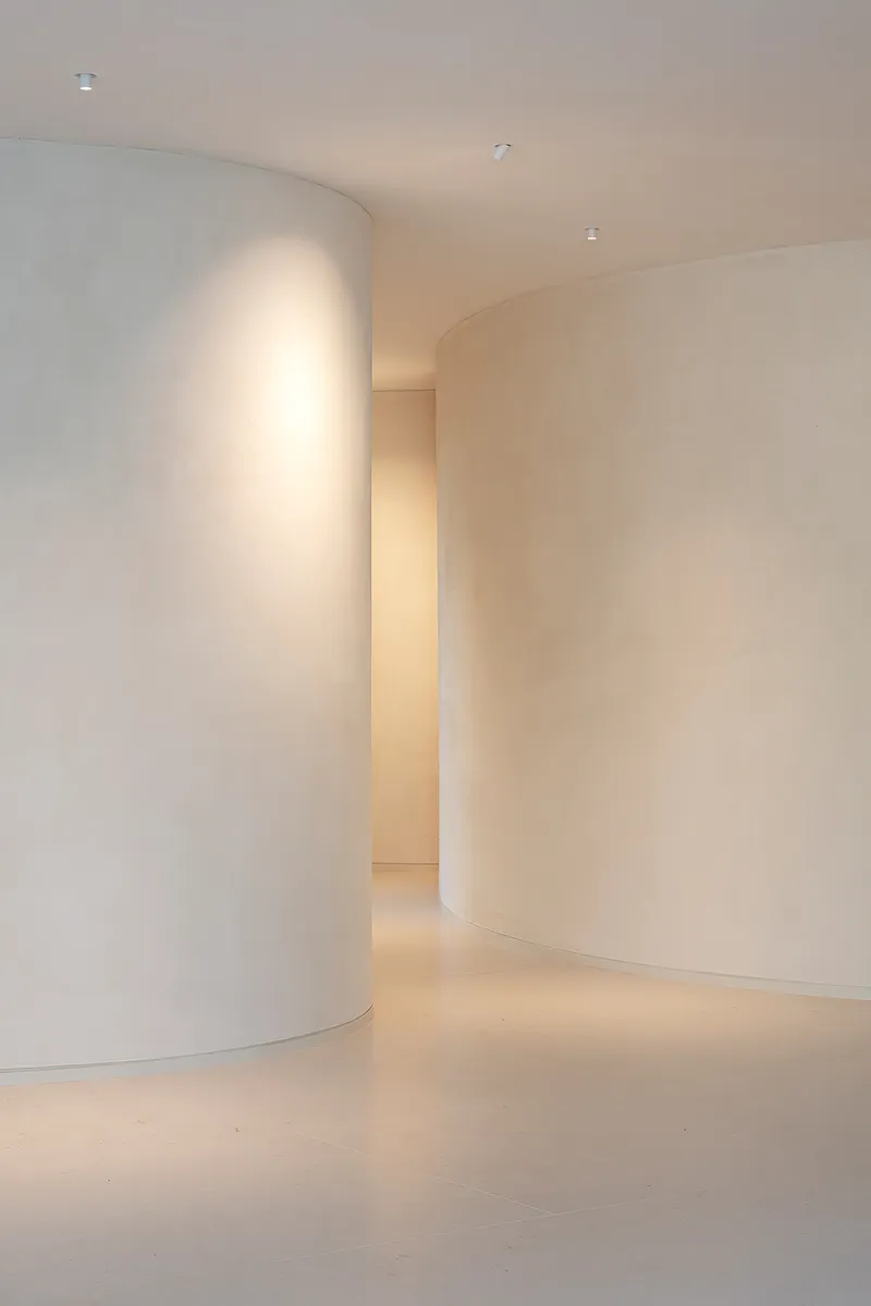 Interior passageway between two tall curved plaster walls with recessed ceiling lighting