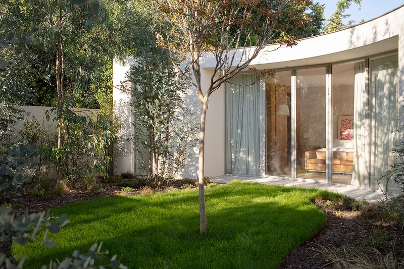 Interior courtyard with lawn, mature trees, and floor-to-ceiling glass walls in afternoon light