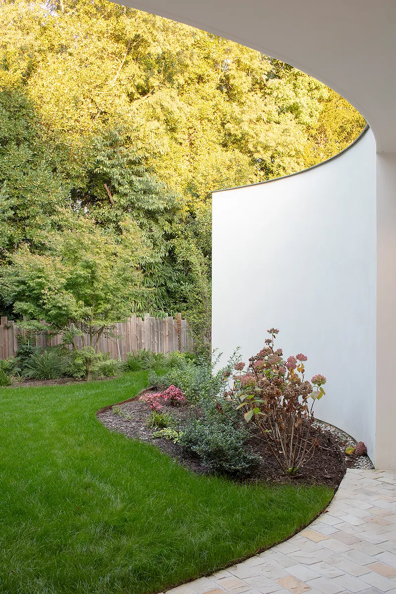 Curved white wall meeting a planted bed and lawn beneath autumn trees