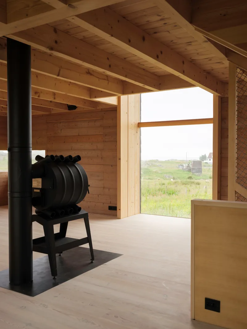 Black cast iron stove on a metal hearth beneath a timber beam ceiling with landscape view beyond