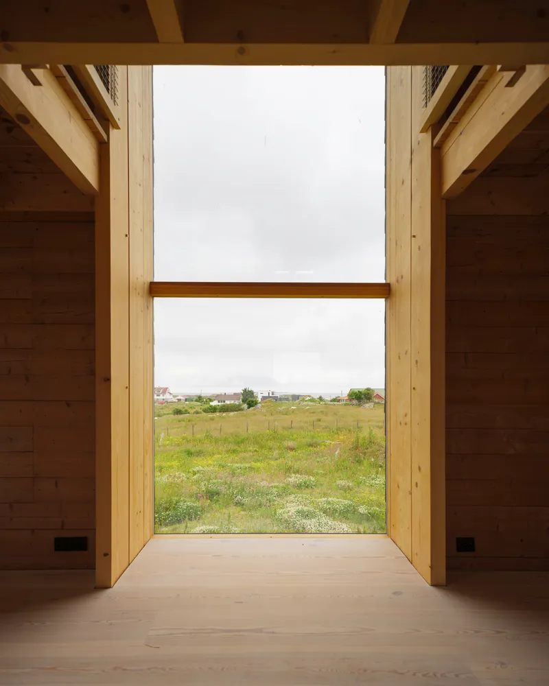 Floor-to-ceiling window framing view of green field with scattered houses under overcast sky
