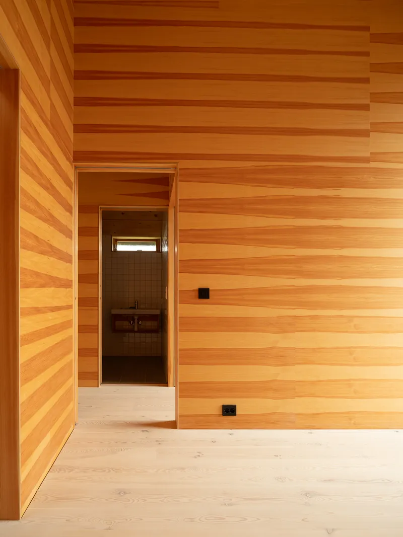 Interior corner with horizontal timber wall cladding and doorway leading to darker room beyond