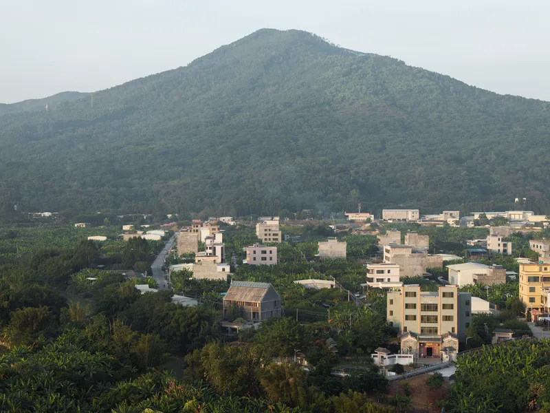 Aerial view of low-rise housing amid dense greenery with forested mountain backdrop