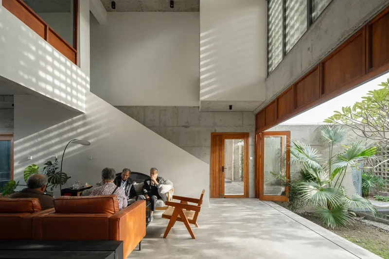 Double-height living room with concrete ceiling, timber doors and patterned light from perforated screens falling across white walls