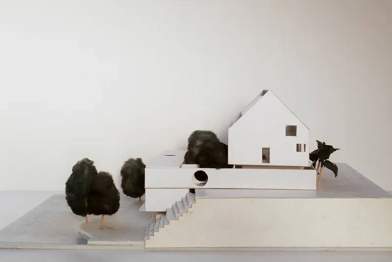 Physical model of a gabled house on a terraced plinth with small trees and steps