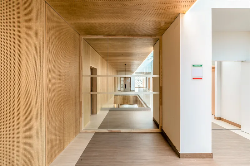 Perforated timber wall and ceiling lining a corridor with view through glass to interior spaces