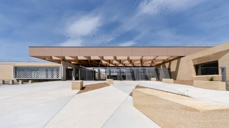 Entrance canopy supported by angled timber columns under a bright midday sky